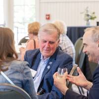 Former President Thomas Haas sitting at table in conversation with woman and gentleman at event